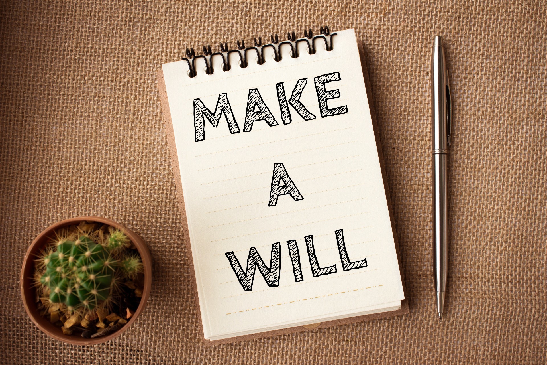 "Make a Will" written on a spiral-bound notepad, with a cactus plant and pen nearby; our Wills Solicitors in Preston can be contacted by completing the form overleaf.